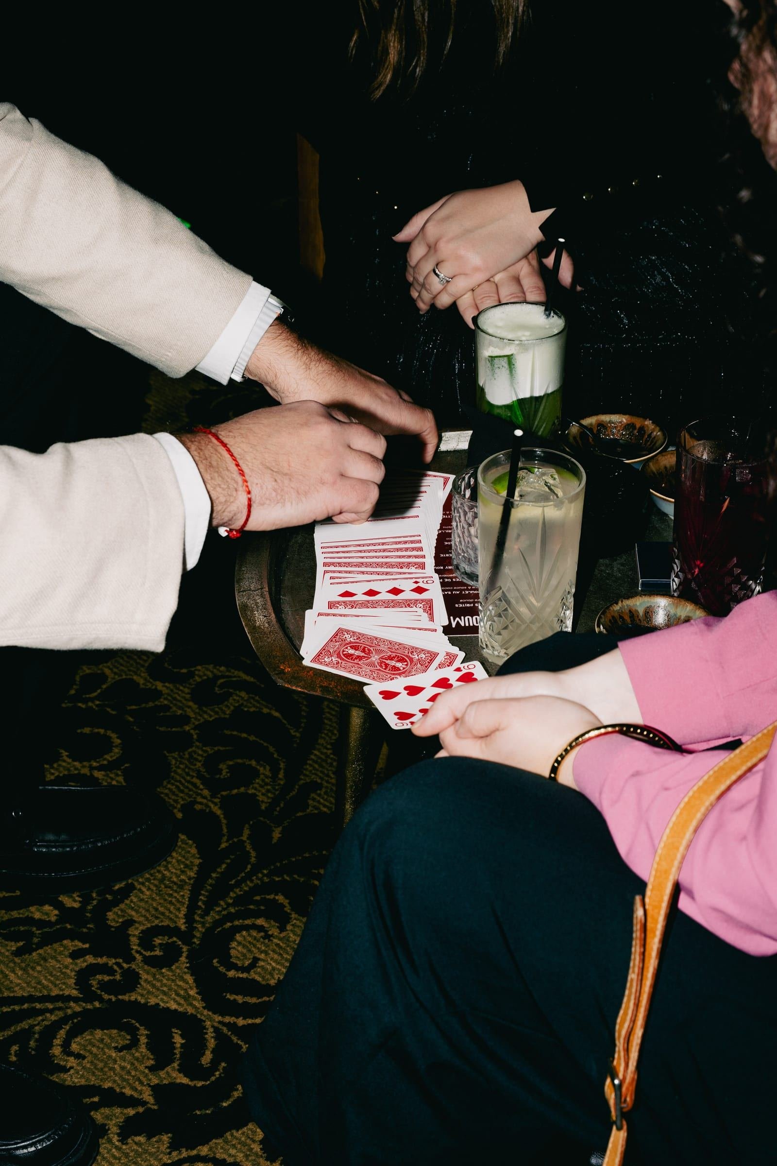 Les mains au-dessus de l'éventail de cartes, entre les verres d'un cocktail