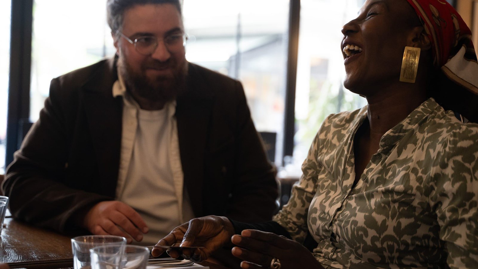À une table de restaurant, deux amis partagent un éclat de rire, une carte à la main