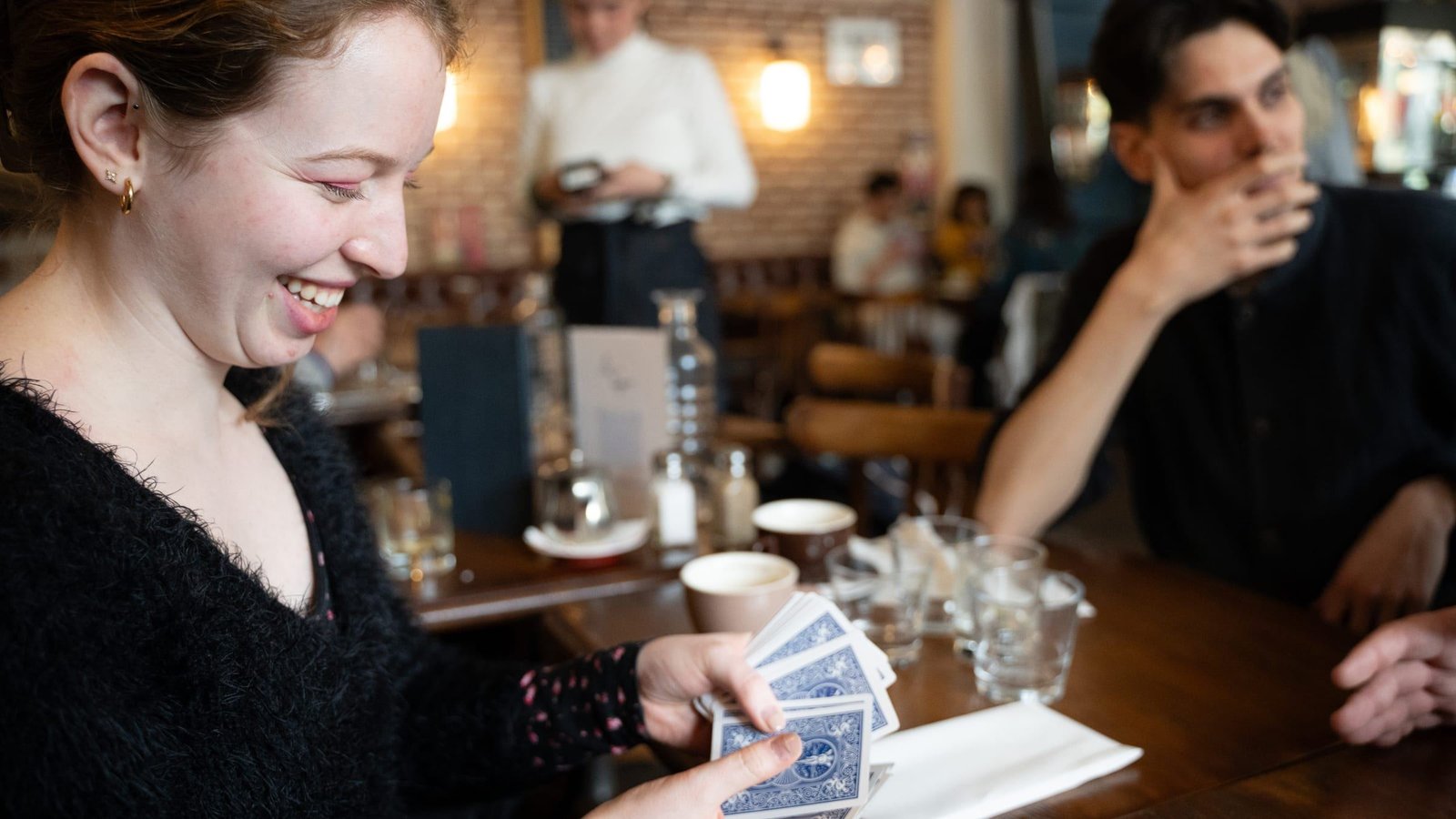 À une table de restaurant, une spectatrice rit aux éclats, des cartes à la main